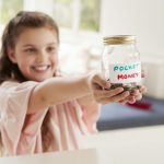 Girl Saving Pocket Money In Glass Jar At Home