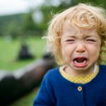 Portrait of small girl outdoors in garden, crying