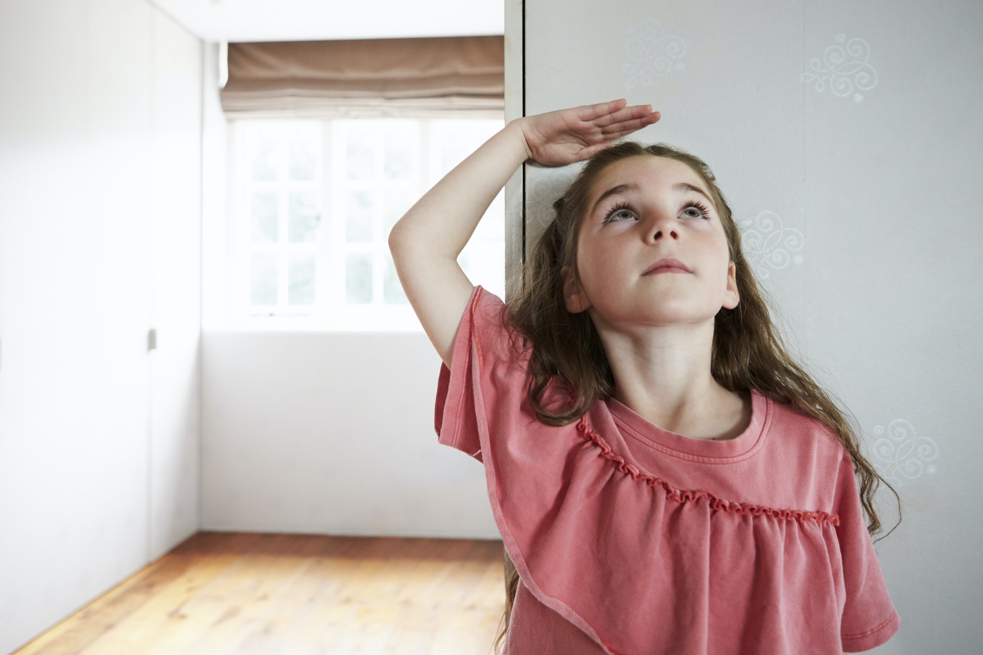 Girl Measuring Height Standing Against Wall At Home