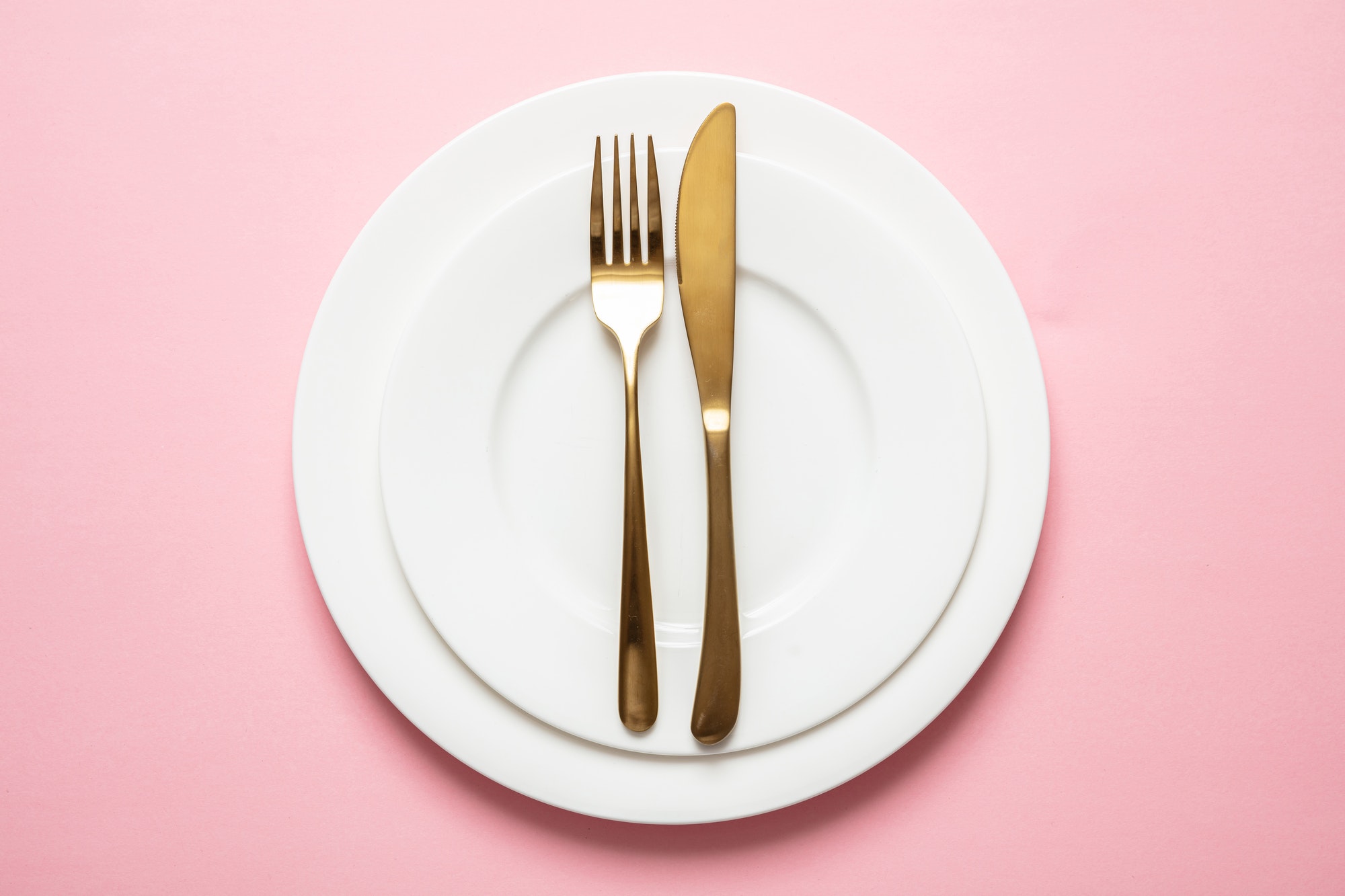 Gold cutlery and dishes set against pink background, formal place setting