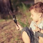 Happy little boy exploring nature with magnifying glass