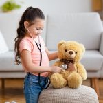 Kid Girl Playing Doctor Using Stethoscope Treating Teddy Bear Indoor