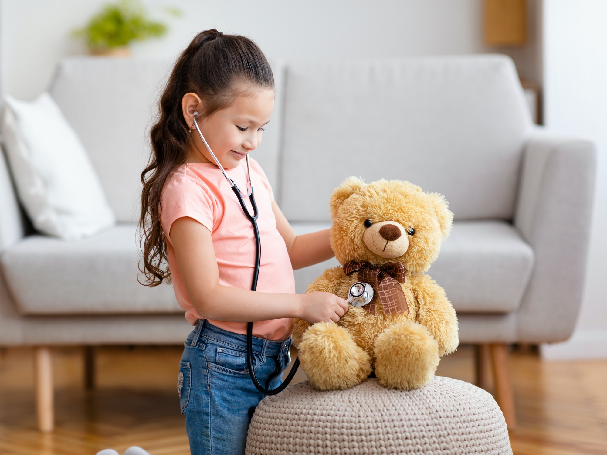 Kid Girl Playing Doctor Using Stethoscope Treating Teddy Bear Indoor