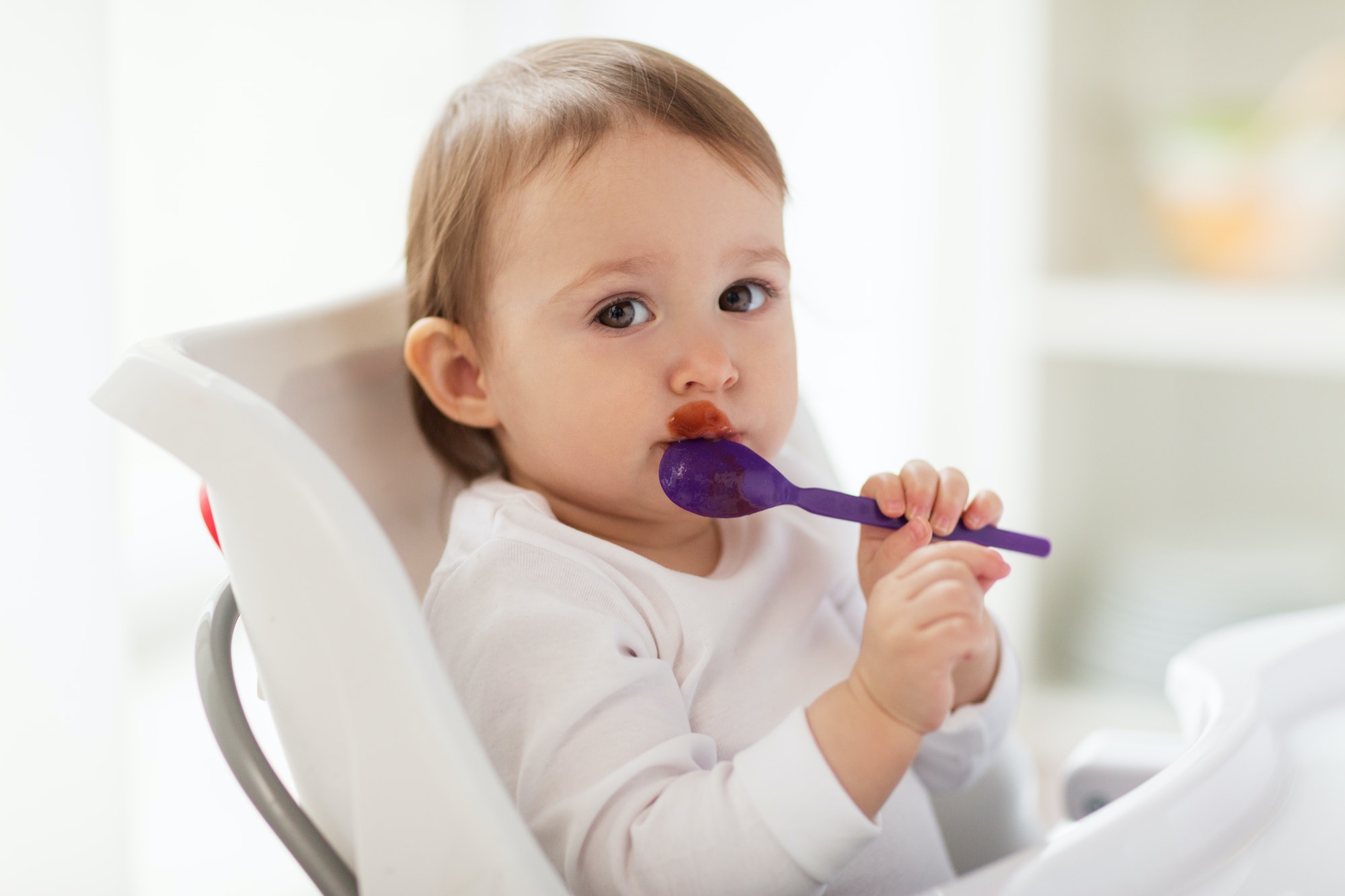 baby with spoon eating food at home