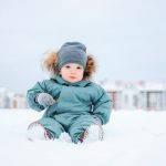Cute baby boy in the mint winter suit sitting on snow outdoor