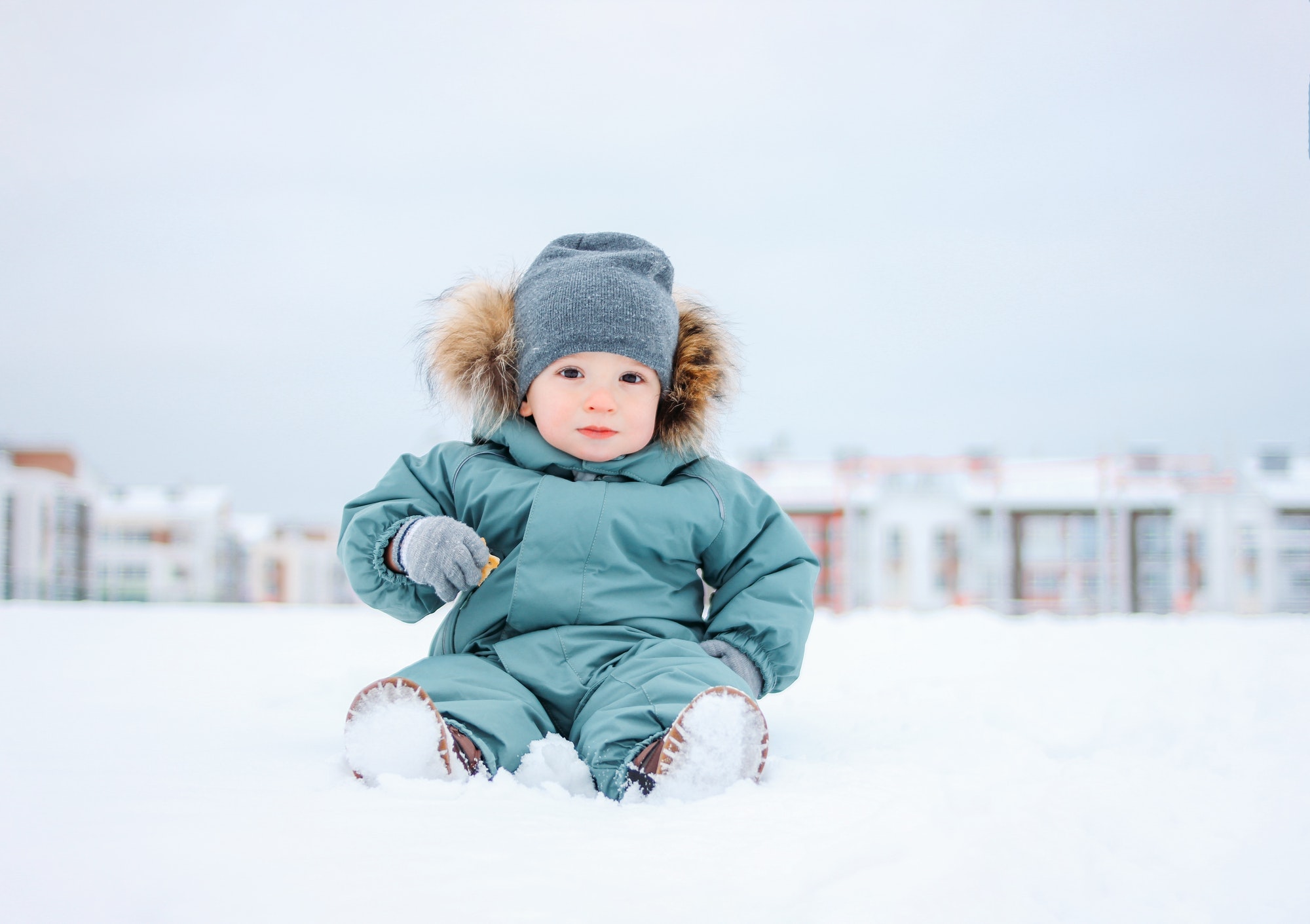 Cute baby boy in the mint winter suit sitting on snow outdoor