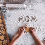 Partial top view of child holding heart shaped cookie and word mom written in flour, Mothers day