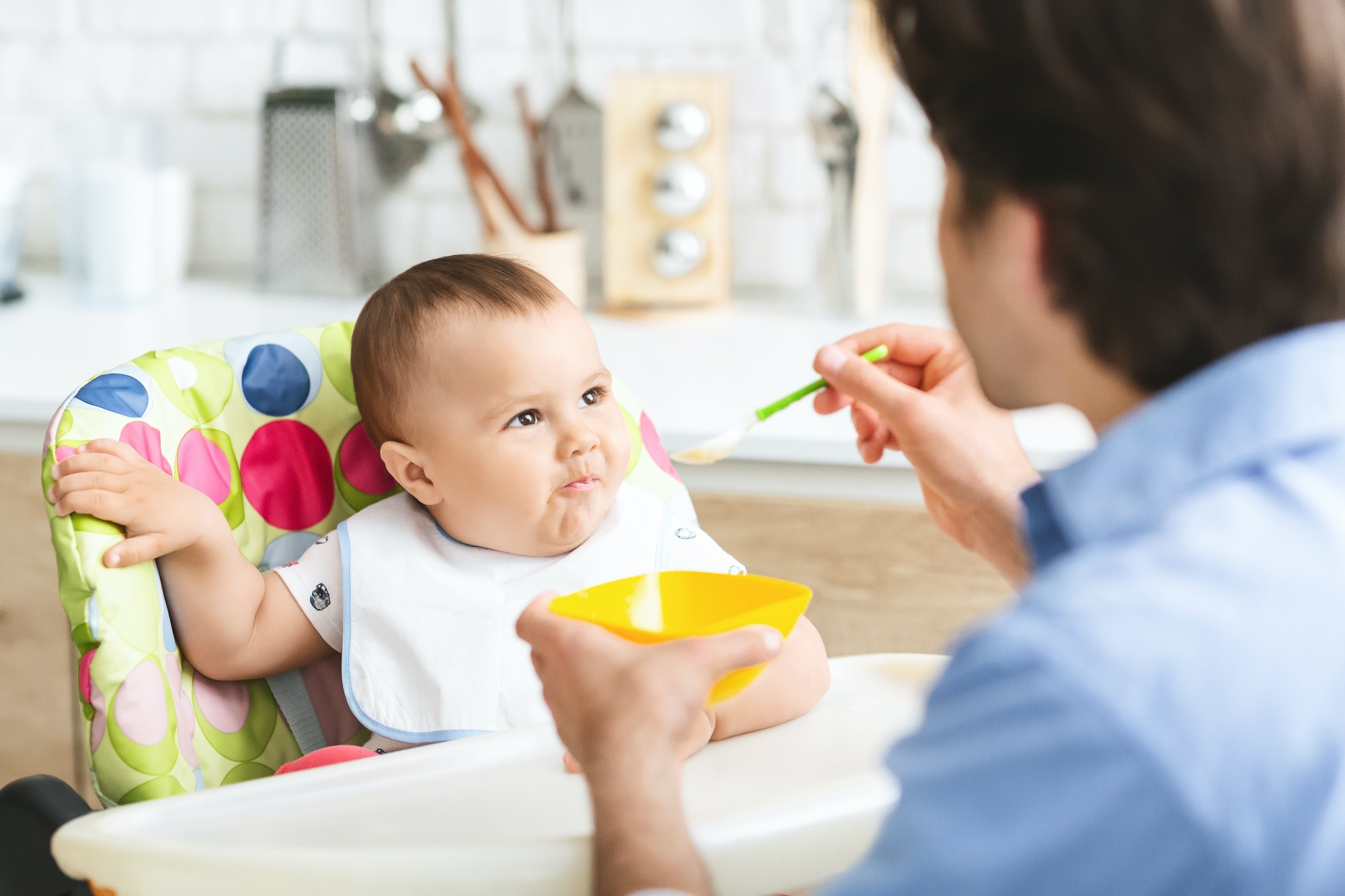 Hungry baby eating healthy kid food in kitchen