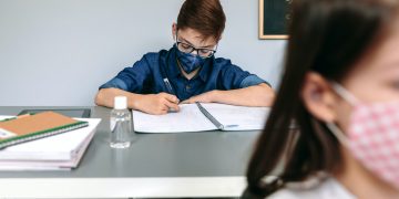 Boy with face mask writing at school