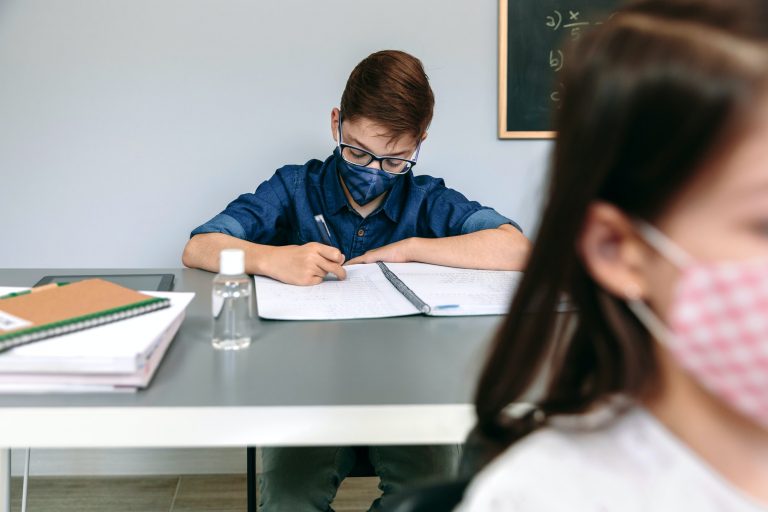 Boy with face mask writing at school