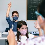 Students with masks raising hands at school