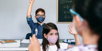 Students with masks raising hands at school