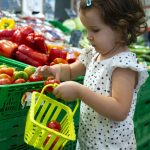 Little girl buying tomatoes in supermarket. Child hold small bas