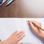 partial view of kid writing in notebook while doing homework