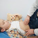 Doctor examining child and doing abdominal palpation
