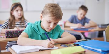 Schoolboy writing in exercise book in class